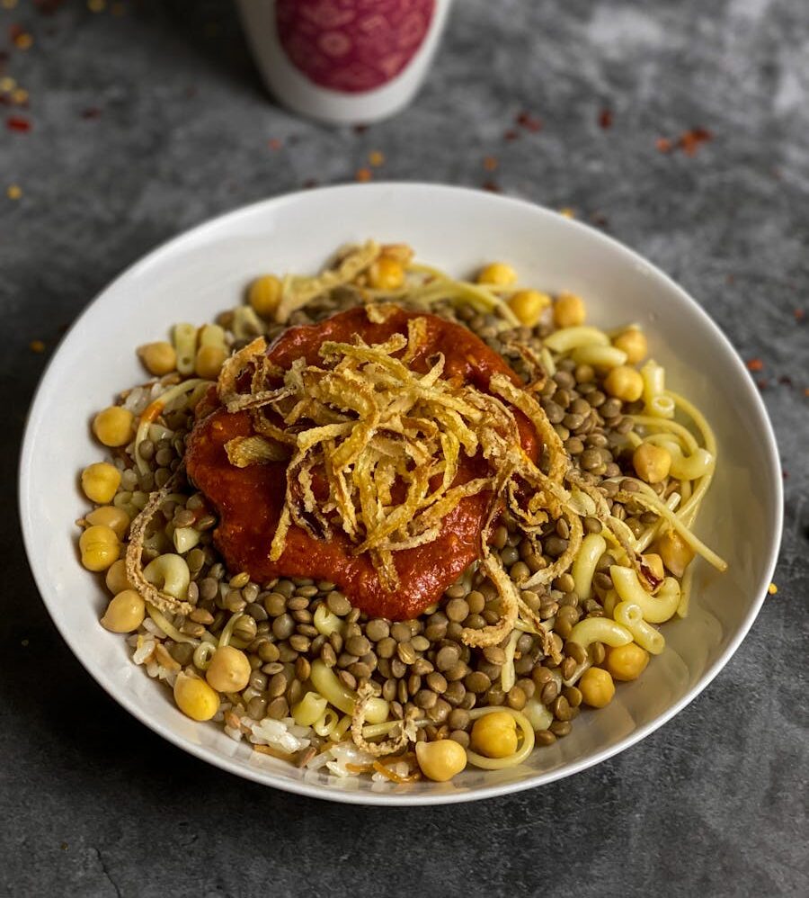Savor the flavors of Koshari, a traditional Egyptian dish with lentils, chickpeas, and tangy tomato sauce.