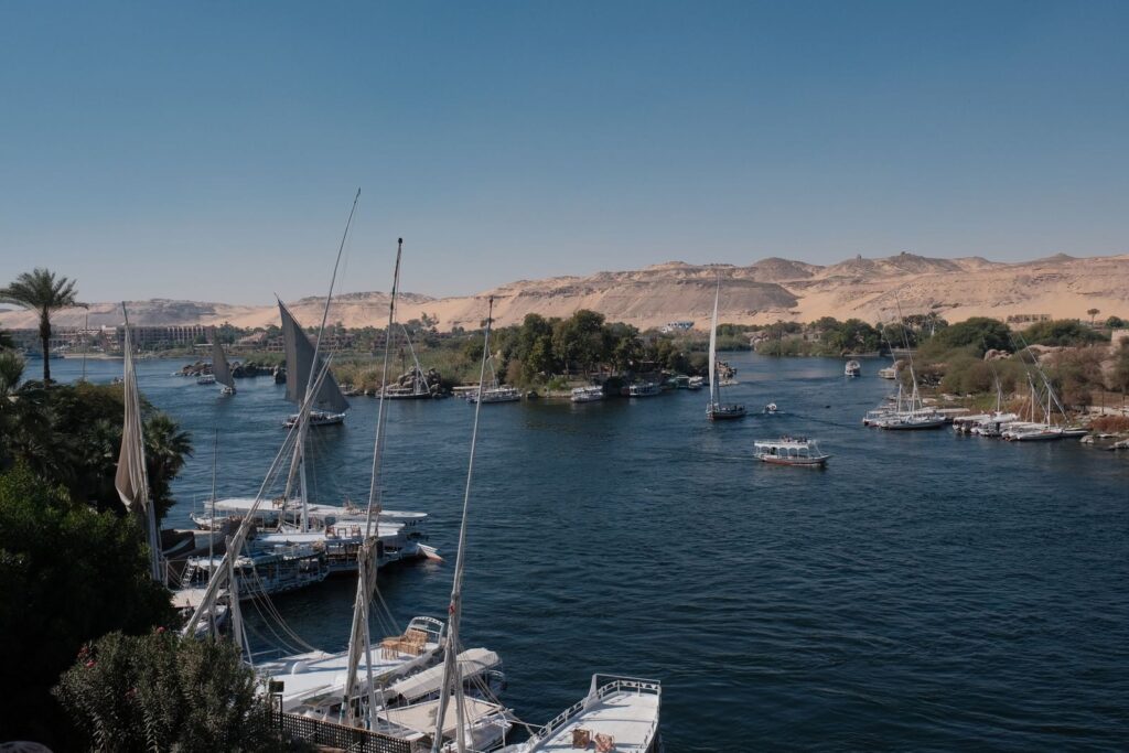 Steamboats and sailboats navigate the scenic Nile River with desert hills in the background, Egypt.