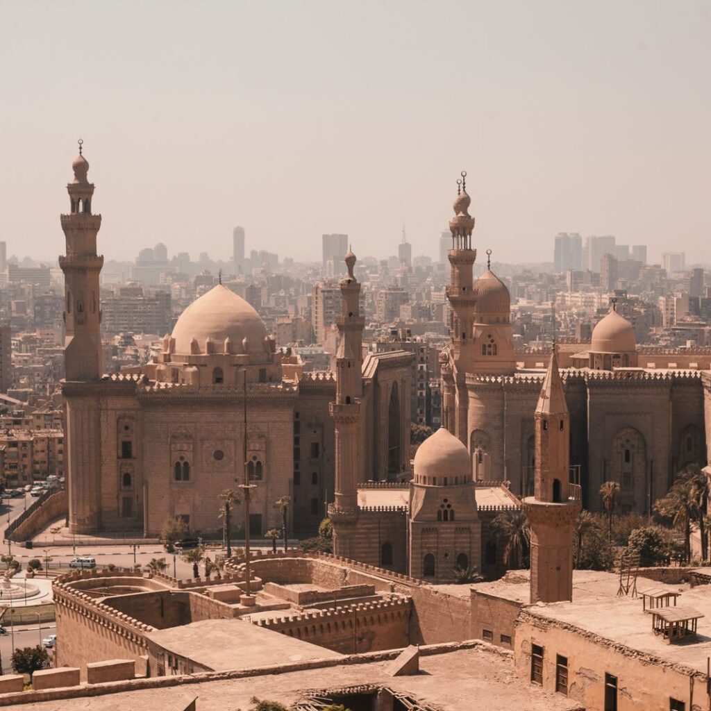 Aerial view of Cairo's historic mosques with a modern skyline backdrop under a clear sky.