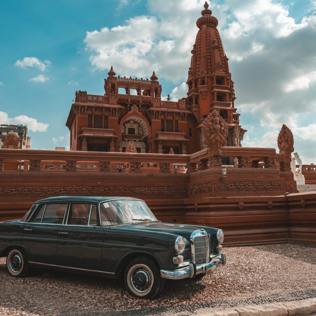 A classic vintage car parked in front of an ornate historic palace under a blue sky.